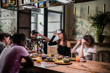 Positive emotional beautiful girl with her smartphone on her forehead sitting at the table with friends and trying to guess a word written on her display.