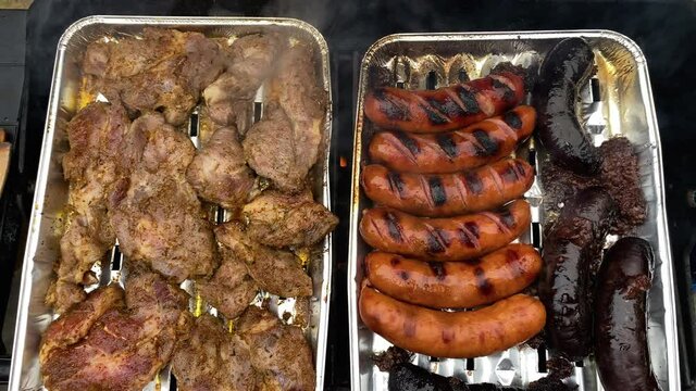 Grilling Marinated Pork, Chicken, And Blood Sausages On An Aluminum Foil Trays Over Medium Fire. - high angle shot