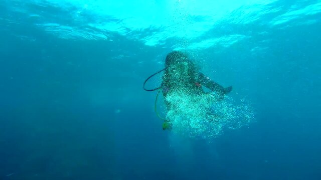 Female scuba diver playing with scuba bubbles in the deep blue (slow motion)