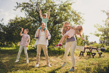 Full body size photo of big full family five people three little kids gathering son dad piggyback mom play daughter relax picnic table on summertime day green house garden backyard outdoors
