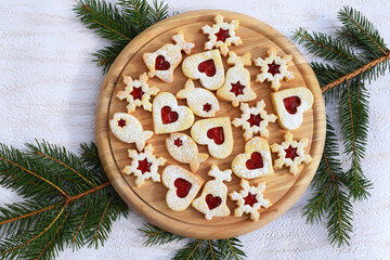 Obraz na płótnie Canvas Homemade linzer cookies filled with strawberry jam on round wooden board and spruce twig. Top view