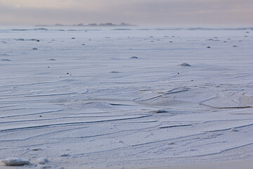 Winter minimalistic landscape with frozen coast and horisont in pastel pink and blue color with lines, strapes on ice, wind and little island far away.