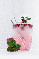 Cold berry lemonade with red bilberry, straws and ice in sunlight  on soft light white wood table, vertical, closeup.