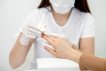 Manicure master applying warm wax from candle on fingernails of young woman in nail salon