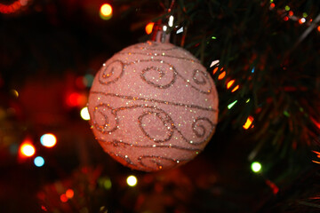 White Christmas ball with a beautiful pattern hanging on a branch of a fir tree. Christmas background with Christmas tree decoration.