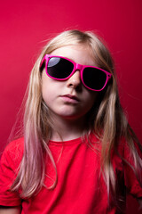 Naklejka premium Studio portrait of a young girl wearing red t shirt and pink sunglasses on red background.