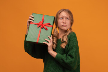 Image of charming blonde girl 12-14 years old holding present box with red bow. Studio shot, yellow background, isolated