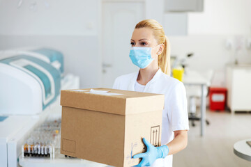 Attractive positive blond lab assistant carrying box with vaccines for Covid 19. Laboratory...