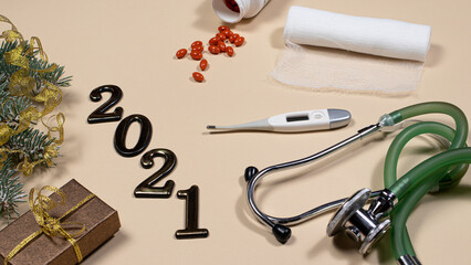 New Year's card on medical subjects: figures 2021, phonendoscope, tablets, thermometer and bandage with spruce branch on a beige background. New Year 2021 medicine.