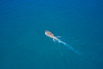 Speed boat movement at high speed aerial view. High-speed yacht of white color fast motion on blue water in the rays of the sun top view. Top back view of the boat.