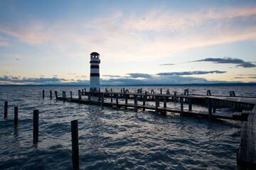 Lighthouse at the end of jetty on the shores of a large lake during dusk

