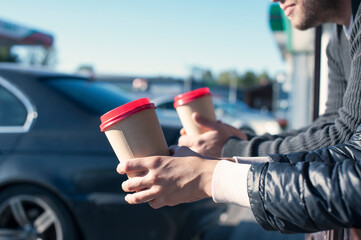 The girl with the guy at the gas station drinks coffee on the background of the car.