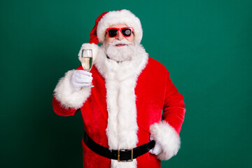 Portrait of his he nice attractive handsome cheerful cheery Santa father drinking champagne having fun saying congrats toast festive day isolated over green color background