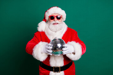 Portrait of his he nice attractive handsome cheerful Santa grandfather mc pj father having fun holding in hands silver glossy ball newyear celebratory good mood isolated over green color background