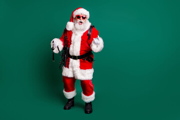 Full length body size view of his he attractive cheerful crazy cool bearded funky funny Santa grandfather holding in hands whip tools showing horn sign having fun isolated green color background