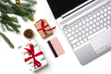 Christmas online shopping. An open laptop on a white background, a credit card, gift boxes tied with a red ribbon, green fir branches, garlands of stars. Online trading during the winter holidays