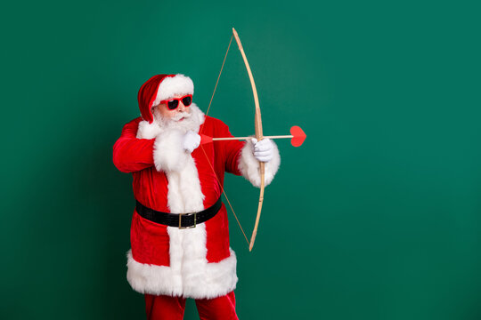 Bullseye. Profile photo of pensioner grandpa hold bow aiming quarreling people shoot arrow heart shapes wear red santa x-mas costume coat gloves sunglass cap isolated green color background
