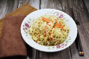 Fried and stirred instant Chinese noodle with sliced fresh cabbage, baby corn and chopped carrot on the plate. Famous vegetarian menu in Asia restaurant.