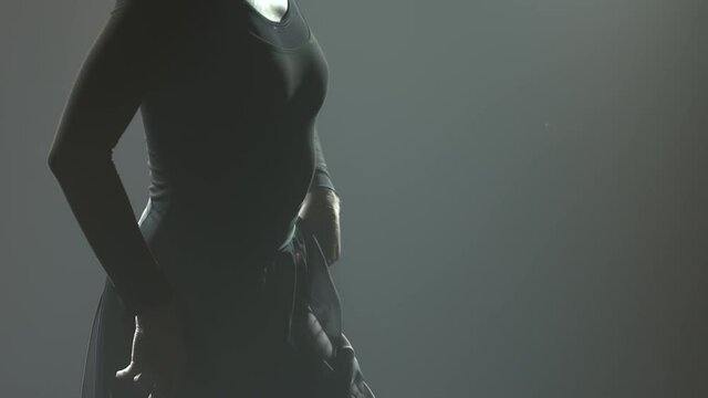 A silhouette of a flexible woman performing dance contemp elements at dusk. Elegant woman dancing contempt in a dark smoky studio with backlight. Slow motion. Close up.