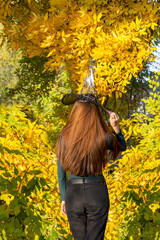Girl with long hair in a pointed witch's hat against a background of yellow autumn trees