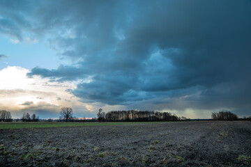 Fototapeta na wymiar Dark rain cloud over a plowed field