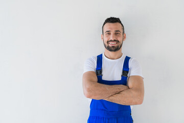 A workman in a blue overalls stands with folded arms on his chest and smiling