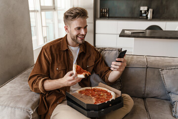 Man eating pizza while using mobile phone