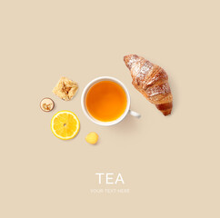 Creative layout made of tea, croissant and lemon on the beige background. Flat lay. Food concept.