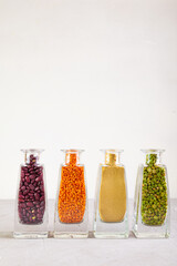 Dried green peas, orange lentils, red beans flowing out of crystal cleasr bottles on to grey concrete surface. Vertical. Copy space