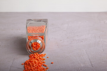 Dried orange lentils flowing out of crystal clear bottle on to grey concrete surface. Horizontal. Copy space. Selective focus.