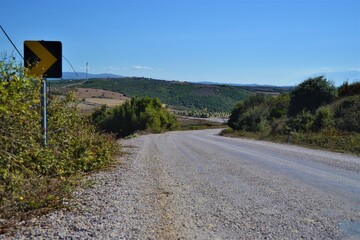 Gravel road in the villages. Blue sky and plants near the gravel roads and small hills.