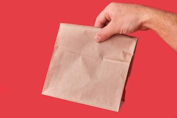 In the man's hand is a package made of a craft brown eco-bag. Red background. Package without logos, food delivery.