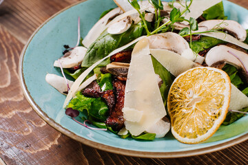 Salad with grilled meat, mushrooms and herbs on wooden background