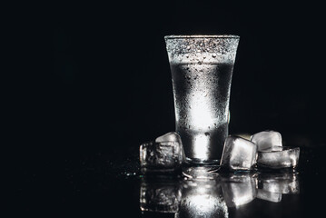 Vodka in shot glasses on black background, iced strong drink in misted glass