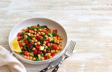 Healthy vegan salad with chickpeas, tomatoes, cucumbers, bell peppers and kale on light wooden background, space	