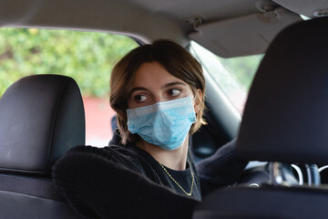 Young woman with surgical mask looking back to park in a car