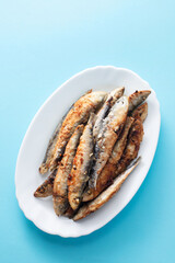 fried small sardines on white dish on blue background