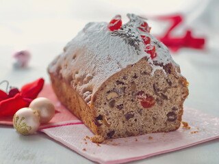 Christmas cake with fruits and nuts. Pound cake decorated with red ribbon, sugar powder and dried cranberries upon white background. Selective focus.