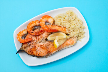 fried salmon with shrimps and cous-cous on white dish on blue background
