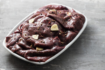 raw liver with black pepper and garlic on the white dish on ceramic background