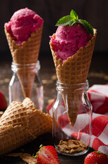 Wafer cones with strawberry icecream in two glass bottles on wooden kitchen table