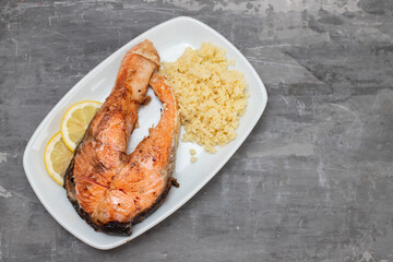 fried salmon with cous cous and lemon on white dish