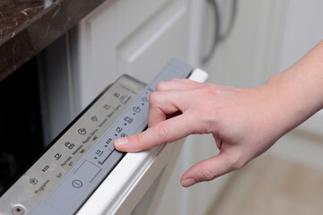 The hand of a woman who opens the dishwasher to insert dirty dishes. The button that presses indicates the economy function, an important indication for safeguarding our environment.