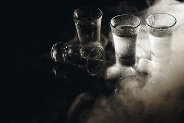 Close-up view of bottle and glasses of vodka standing isolated on black