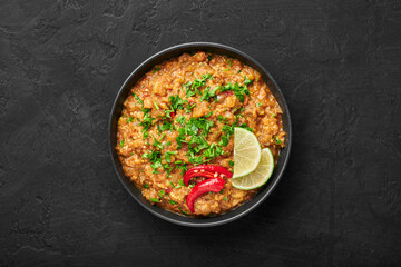 Baingan Bharta or Roasted Mashed Eggplant in black bowl on dark slate table top. Bhurta is indian cuisine puree dish of fire roasted eggplant and masala. Top view