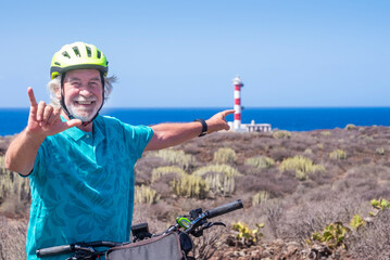 Cheerful bearded senior man with yellow helmet enjoying excursion with bicycle close to a...