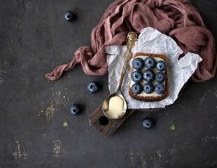 Blueberry sandwich with whipped honey and a spoon with whipped honey on white paper on a dark background with space for text. Top view. Flat lay