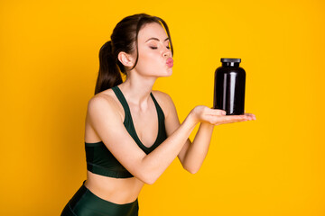 Portrait of attractive dreamy girl holding on palm pills healthy product sending air kiss isolated over bright yellow color background