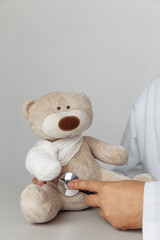 Pediatrician concept. Doctor's hand with stethoscope and teddy bear with bandage.