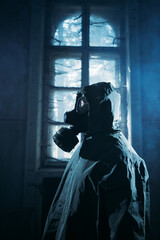 Fototapeta na wymiar Spooky person with gas mask holding a lamp in dense fog in an abandoned building with eerie feeling. 